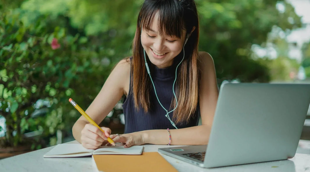 Woman with earphones while writing on a journal