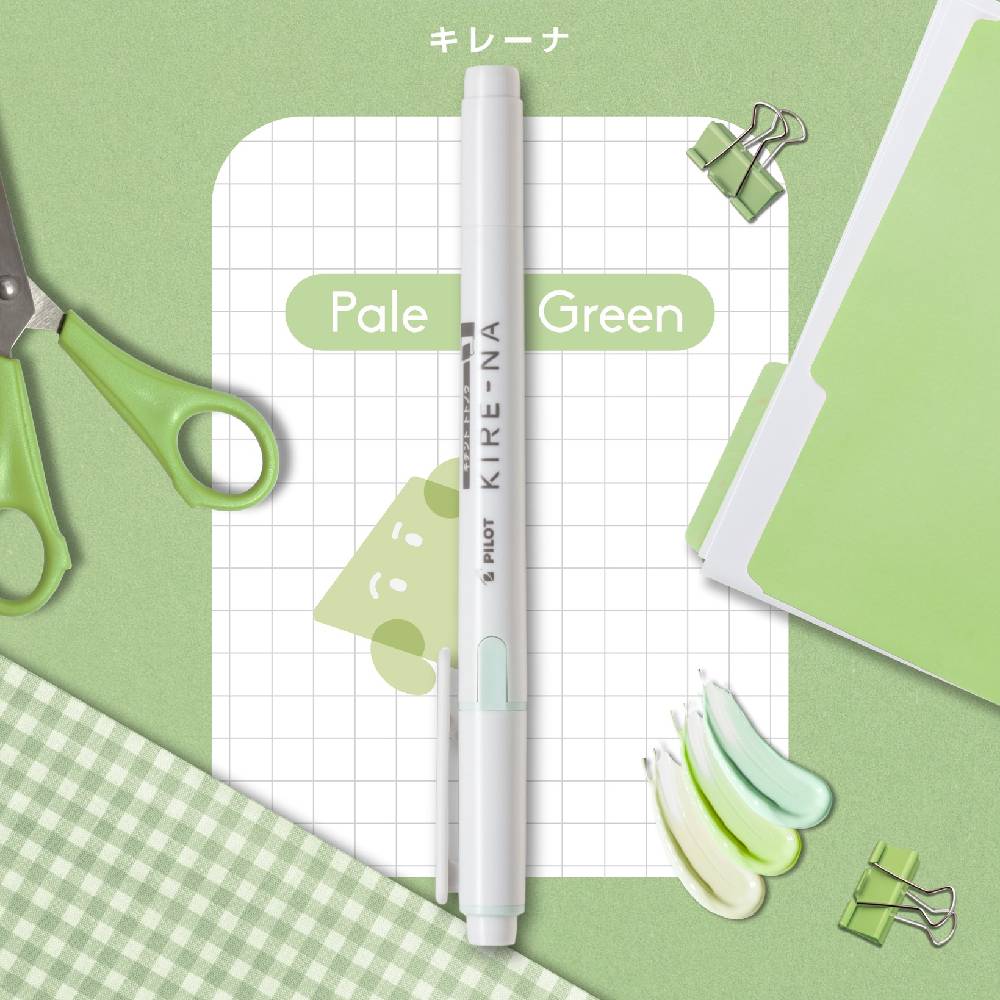Kure-NA pen on a grid paper with scissors and green stationery items on a green background